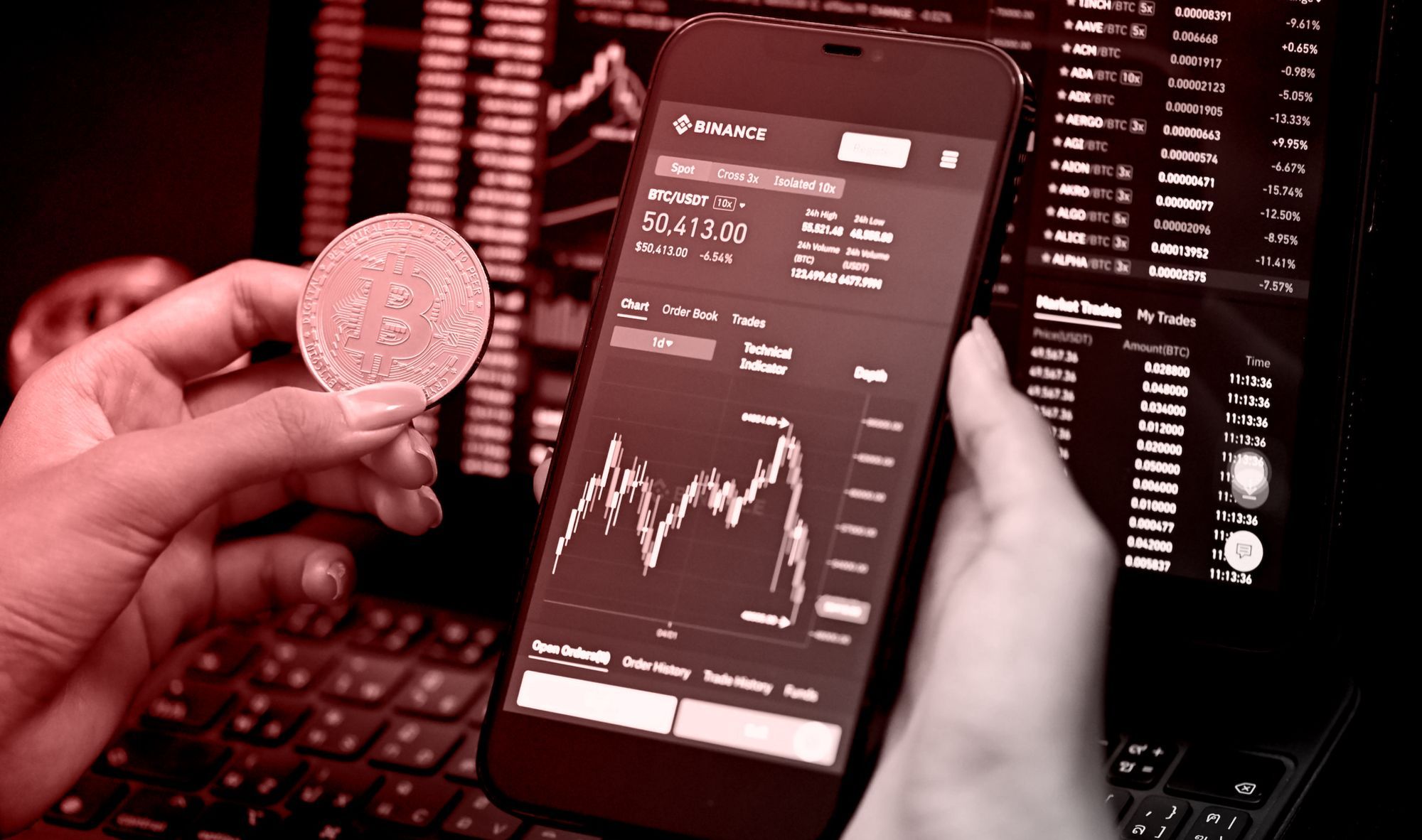 A hand holding a coin with bitcoin logo and a phone opened Binance app showing graph and numbers