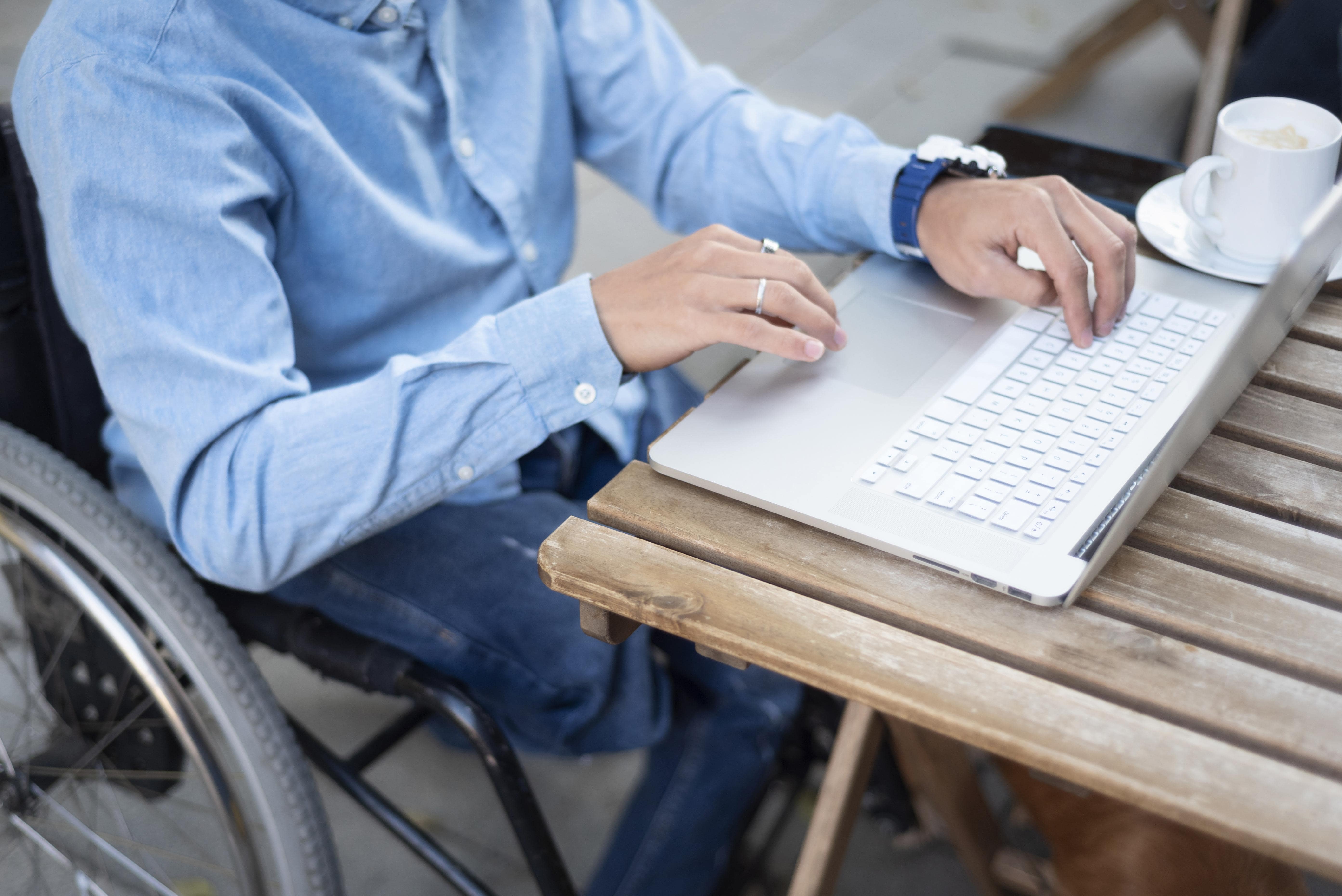 close up disabled man in wheelchair typing on laptop